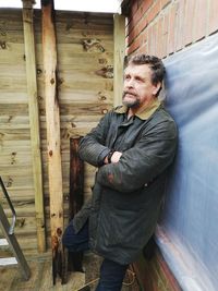 Thoughtful mature man with arms crossed looking away while standing by wall