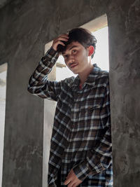 Young man looking away while standing against wall