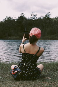 Young woman sitting by lake against trees