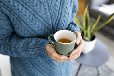 Hands of woman holding cup of tea at home