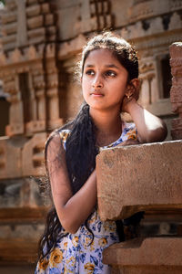 Girl looking away while standing by built structure