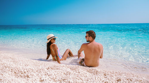 Rear view of woman sitting at beach against clear sky