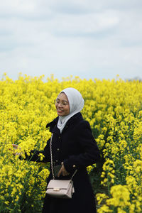 Rear view of woman standing amidst yellow flowering plants on field