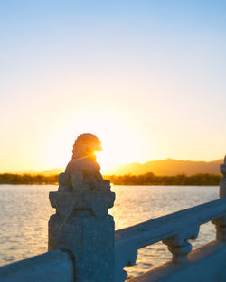 Statue at beach against sky during sunset