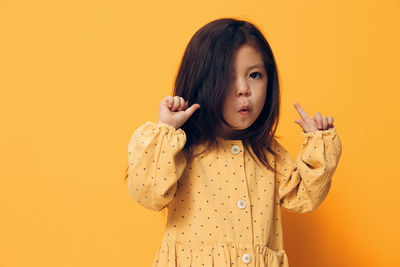 Portrait of young woman standing against yellow background