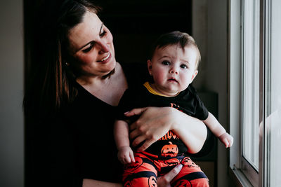 Smiling mother holding daughter sitting by window at home