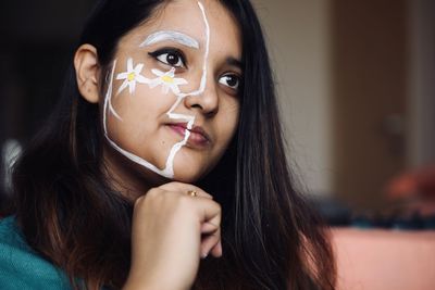 Young woman with face paint looking away sitting at home