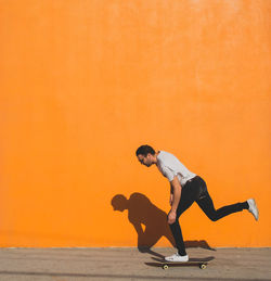 Man skateboarding on street against yellow wall