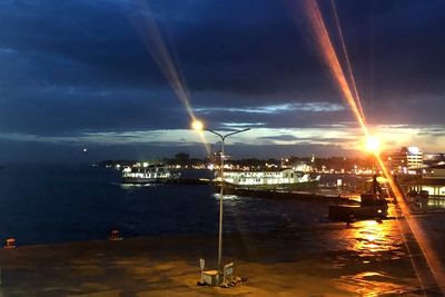 Illuminated city by sea against sky at night