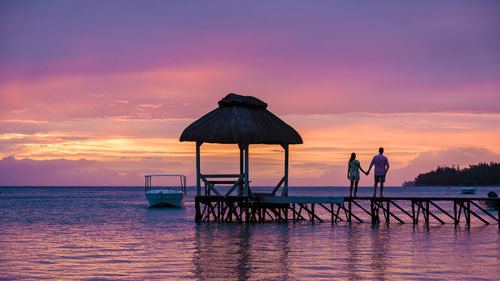 Couple standing on jetty at sunset