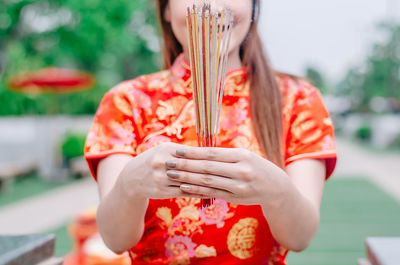 Midsection of young woman in traditional clothing holding incense