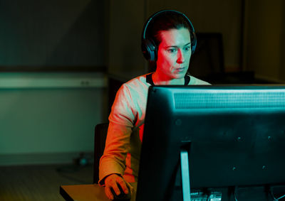 A woman with computer mouse in hand works at computer in dark room