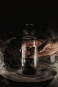 Cropped hand holding stones in bottle amidst smoke at darkroom