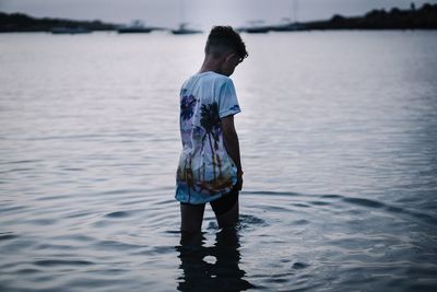 Rear view of boy standing in sea at dusk