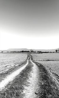 Dirt road on field against clear sky