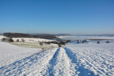 Winter landscape with fields and fog in the valley, with snow, blue sky, germany, bavaria, spessart