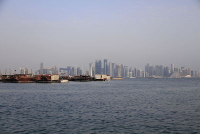 Boats sailing in sea by cityscape against sky