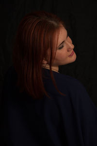 Portrait of woman standing against black background