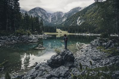 Man standing on rock by lake against mountains