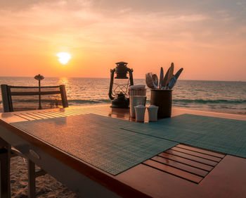 Dining table at beach against sky during sunset