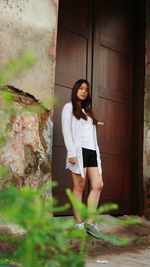 Low angle portrait of young woman standing by wall