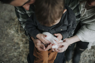 High angle view of son holding rabbit while sitting with parents at farm