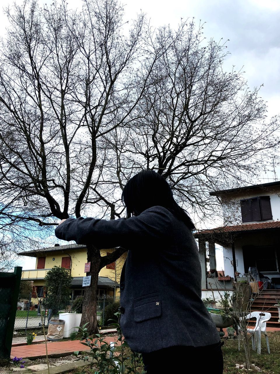 REAR VIEW OF WOMAN STANDING BY BARE TREE AGAINST HOUSE