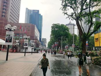 People walking on wet street amidst buildings in city