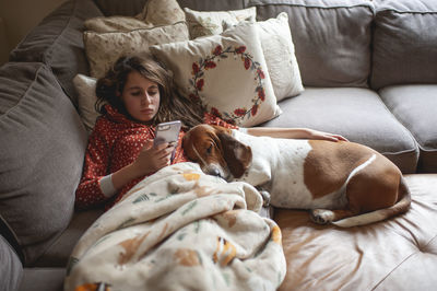 Tween girl looking at her phone while cuddling with hound dog on couch