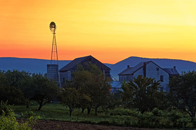 Trees and buildings on field against orange sky