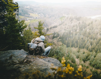 Rear view of hiker sitting on rock looking at trees