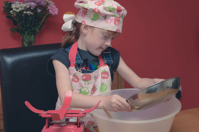 Girl wearing apron mixing flour in container on table at home