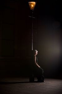 Side view of woman looking away while sitting by pole at night