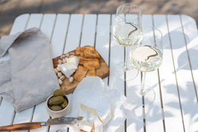 Wine appetizers namely pistachios, camembert cheese, saltine crackers, and olives on a white table.