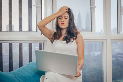 Young woman using phone while standing against window