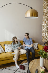 Teenage girl talking with father while sitting on sofa at home