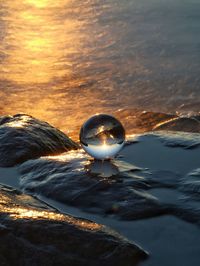 Close-up of crystal ball in sea against sunset sky