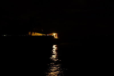 Silhouette built structure by sea against sky at night