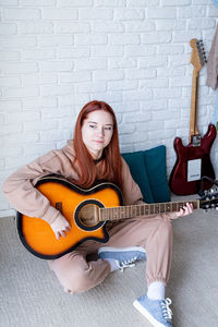 Portrait of woman playing guitar while sitting on sofa at home