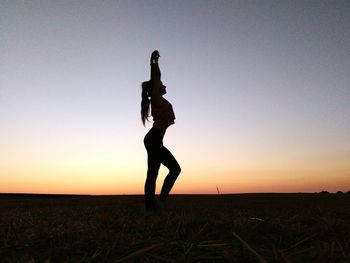 Silhouette woman standing on field against sky during sunset