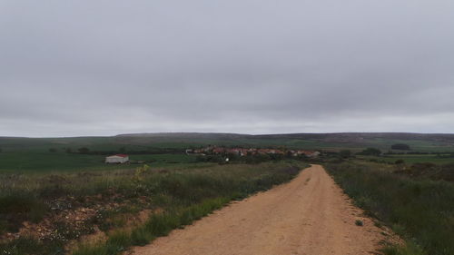 Road passing through field against cloudy sky