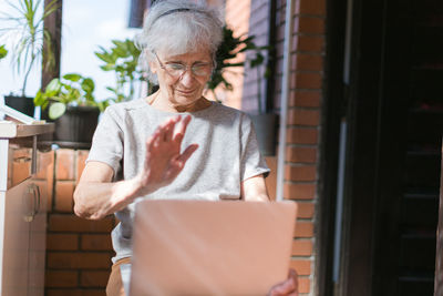 Old woman on her terrace chatting via laptop