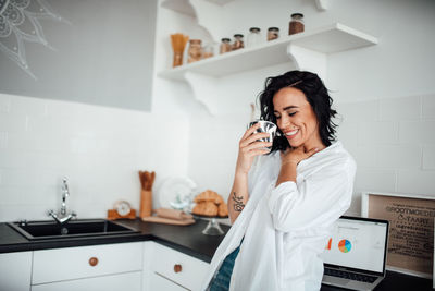 Smiling woman holding coffee cup standing in kitchen