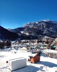 Houses by snow covered mountains against blue sky
