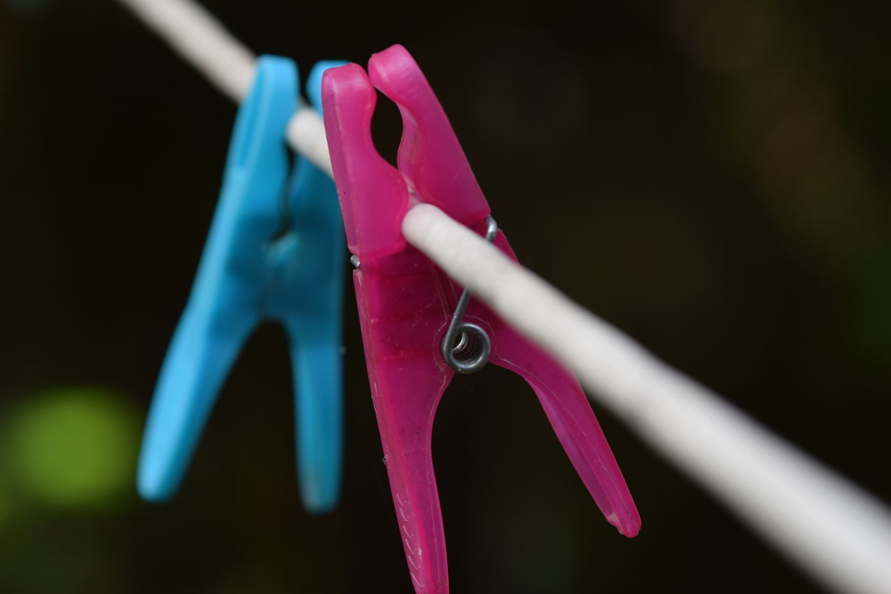 CLOSE-UP OF MULTI COLORED CLOTHESPINS HANGING ON CLOTHESLINE AGAINST BLURRED BACKGROUND