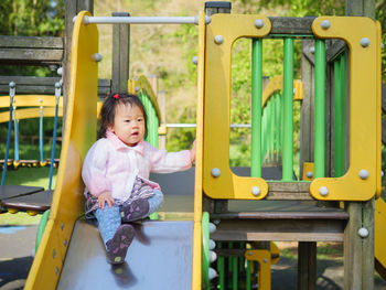 Baby girl sitting on slide at park