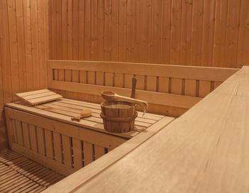 Empty bench with wooden bucket and spoon against wall