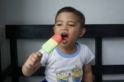 Boy eating flavored ice while sitting on bench