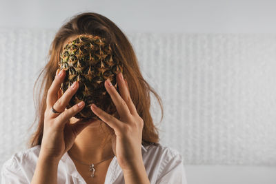 Woman holding pineapple over face at home