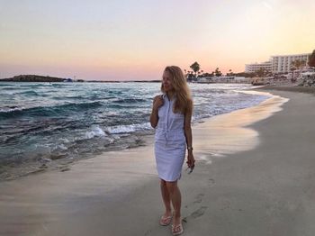 Woman standing at beach against sky during sunset